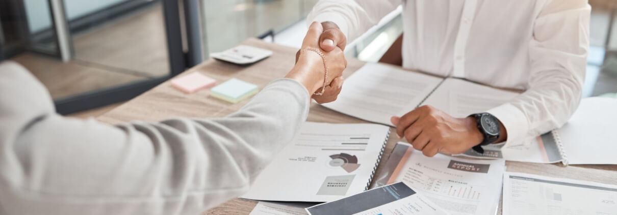 Zwei Menschen schütteln über einem Tisch mit Unterlagen die Hand
